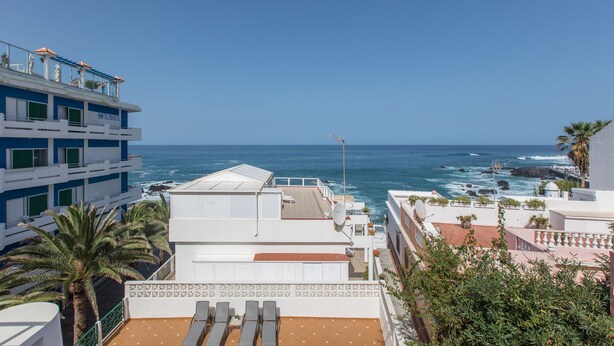 Een hotel met een terras op het dak met uitzicht op de oceaan, met een zwembad en ligbedden.