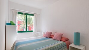 Een slaapkamer met een bed, een nachtkastje, een raam met gordijnen en uitzicht op groen.