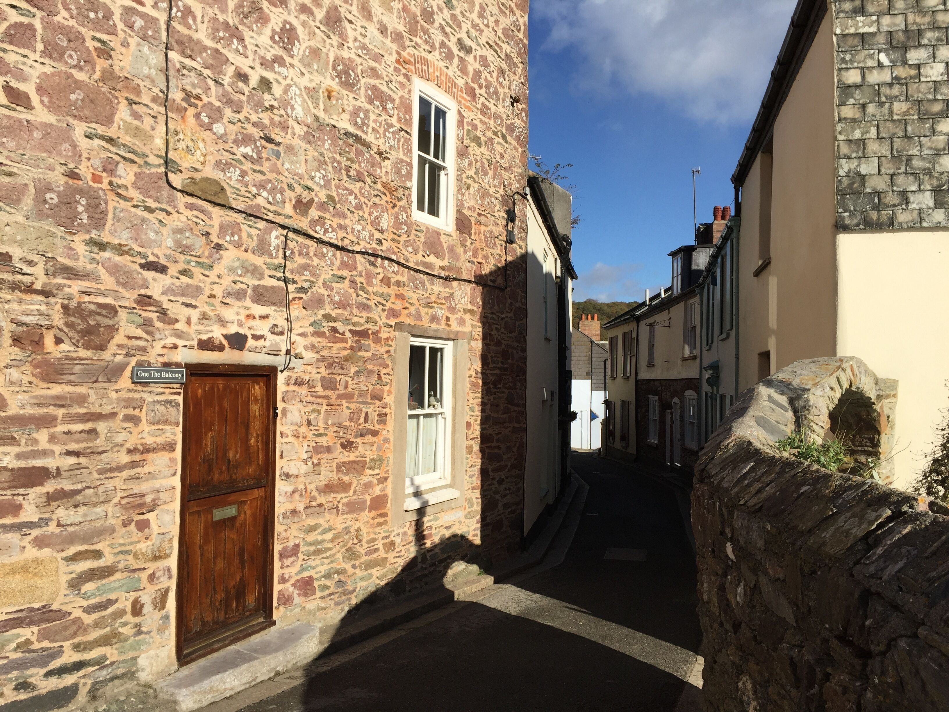 A narrow street with stone buildings, a wooden door, and a sign reading 'One The Balcony'.
