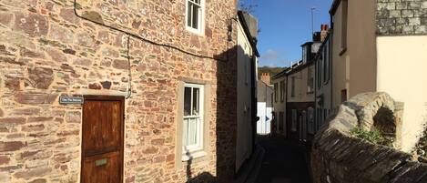 A narrow street with stone buildings, a wooden door, and a sign reading 'One The Balcony'.