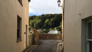 A narrow street with stone walls and a paved road, leading to a house with a visible window and a stone archway. - HOWTON COTTAGE - village cottage on coast path next to beaches (Cawsand)