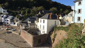A coastal town with buildings on a hillside, a beach with boats, and a stone wall. - HOWTON COTTAGE - village cottage on coast path next to beaches (Cawsand)