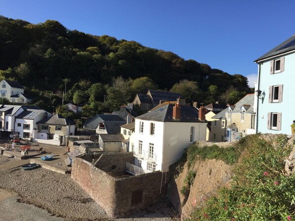A coastal town with buildings on a hillside, a beach with boats, and a stone wall.