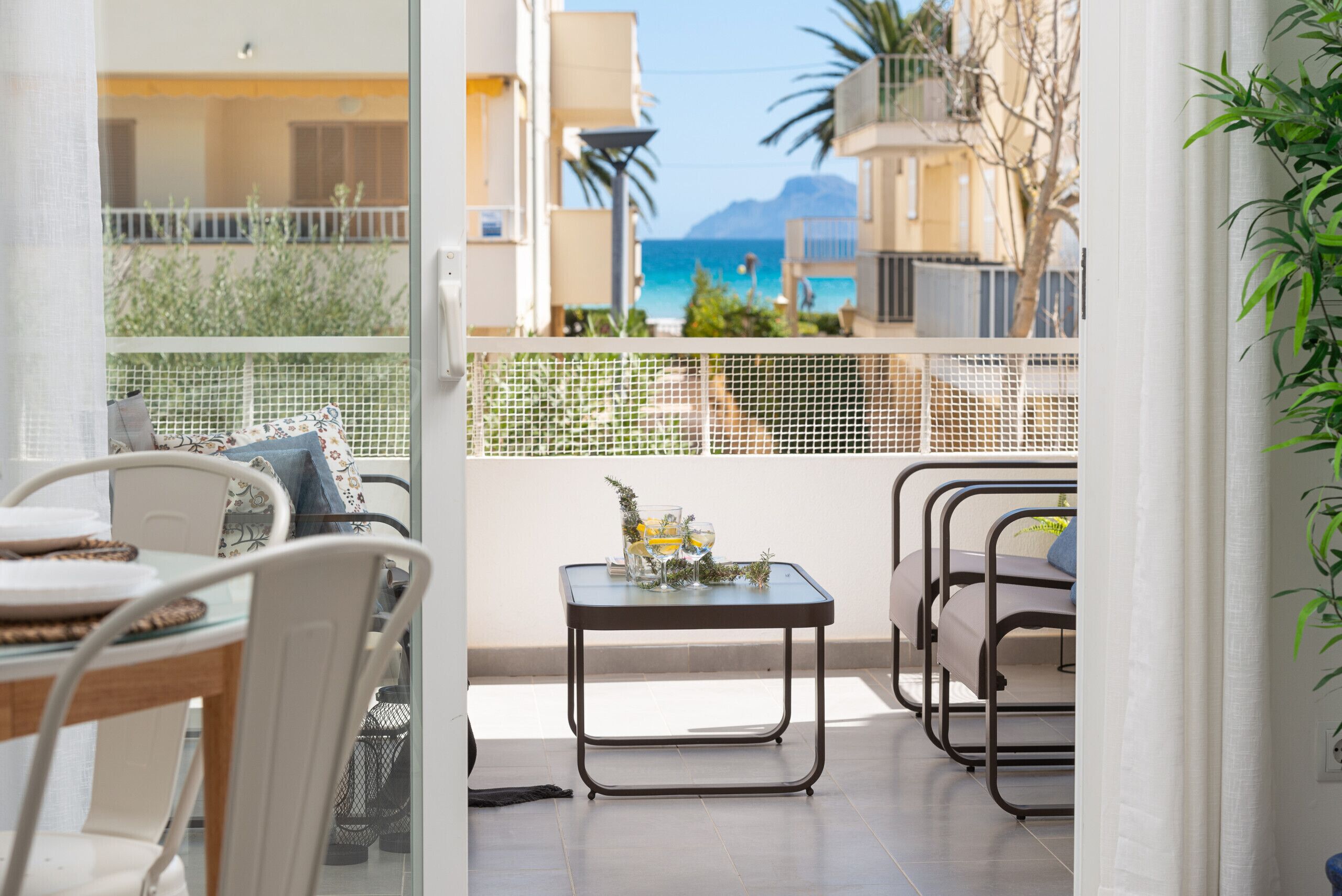 A balcony with a table set for two, a chair, and a view of the sea.