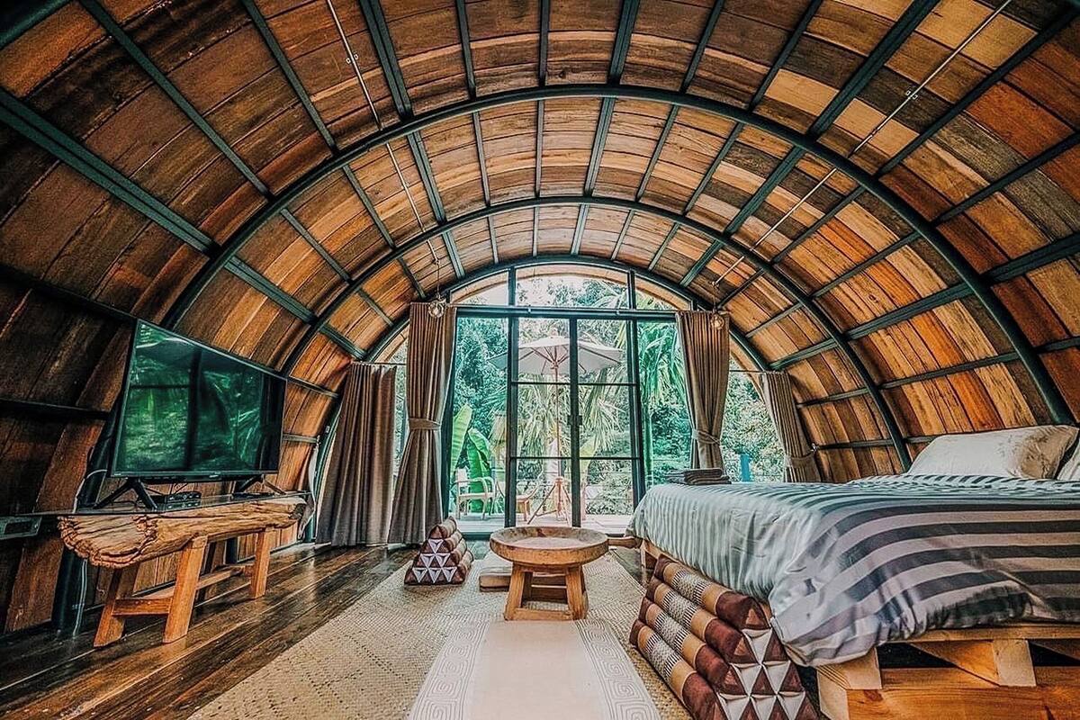 A cozy, arched-roofed room with a bed, a television, and a small table.