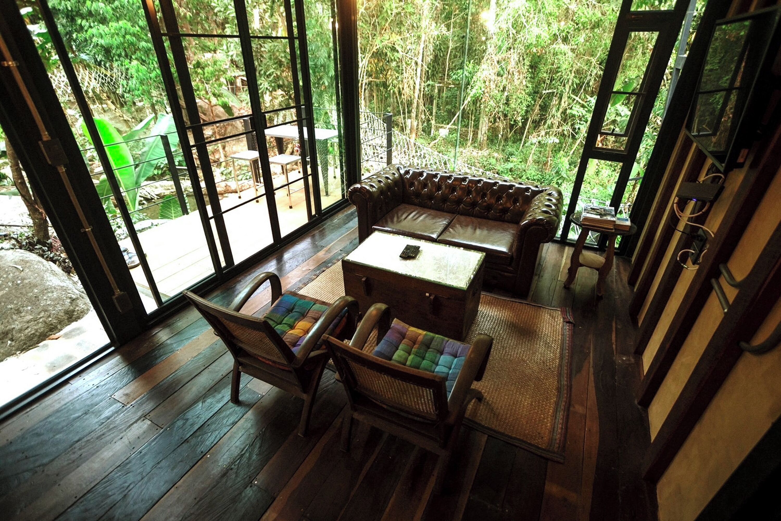 A wooden deck with a leather sofa, two wicker chairs, and a small table.