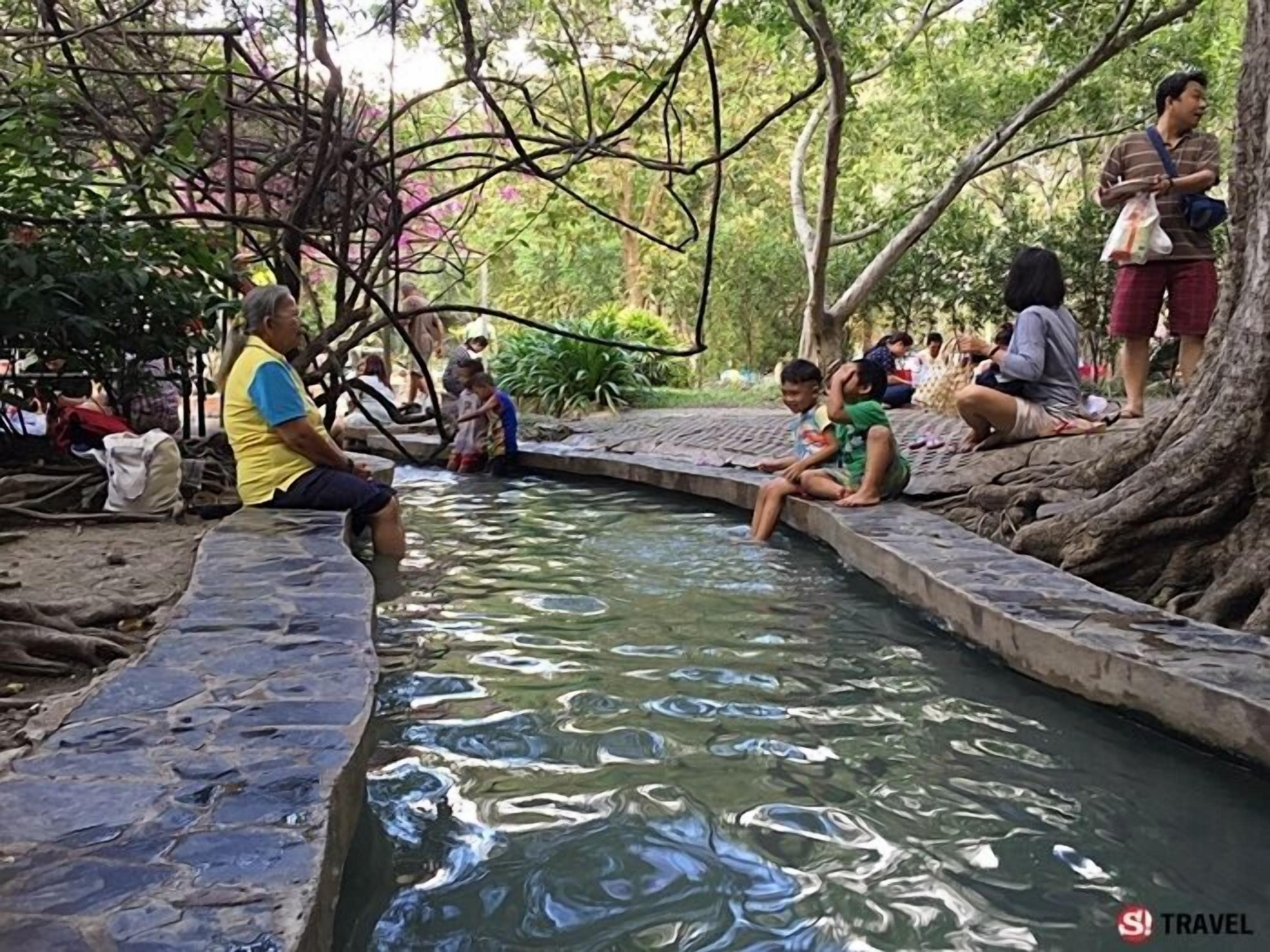 A stone-lined water feature with people sitting and standing around it.