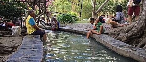 A stone-lined water feature with people sitting and standing around it.