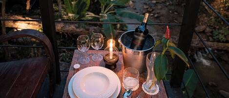 An outdoor dining setup with a table set for two, featuring a bottle of wine, glasses, and a candle.