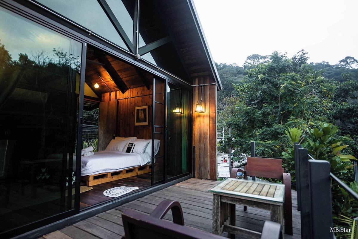 A modern wooden cabin with a glass door leading to a bedroom with a bed and a wooden floor.