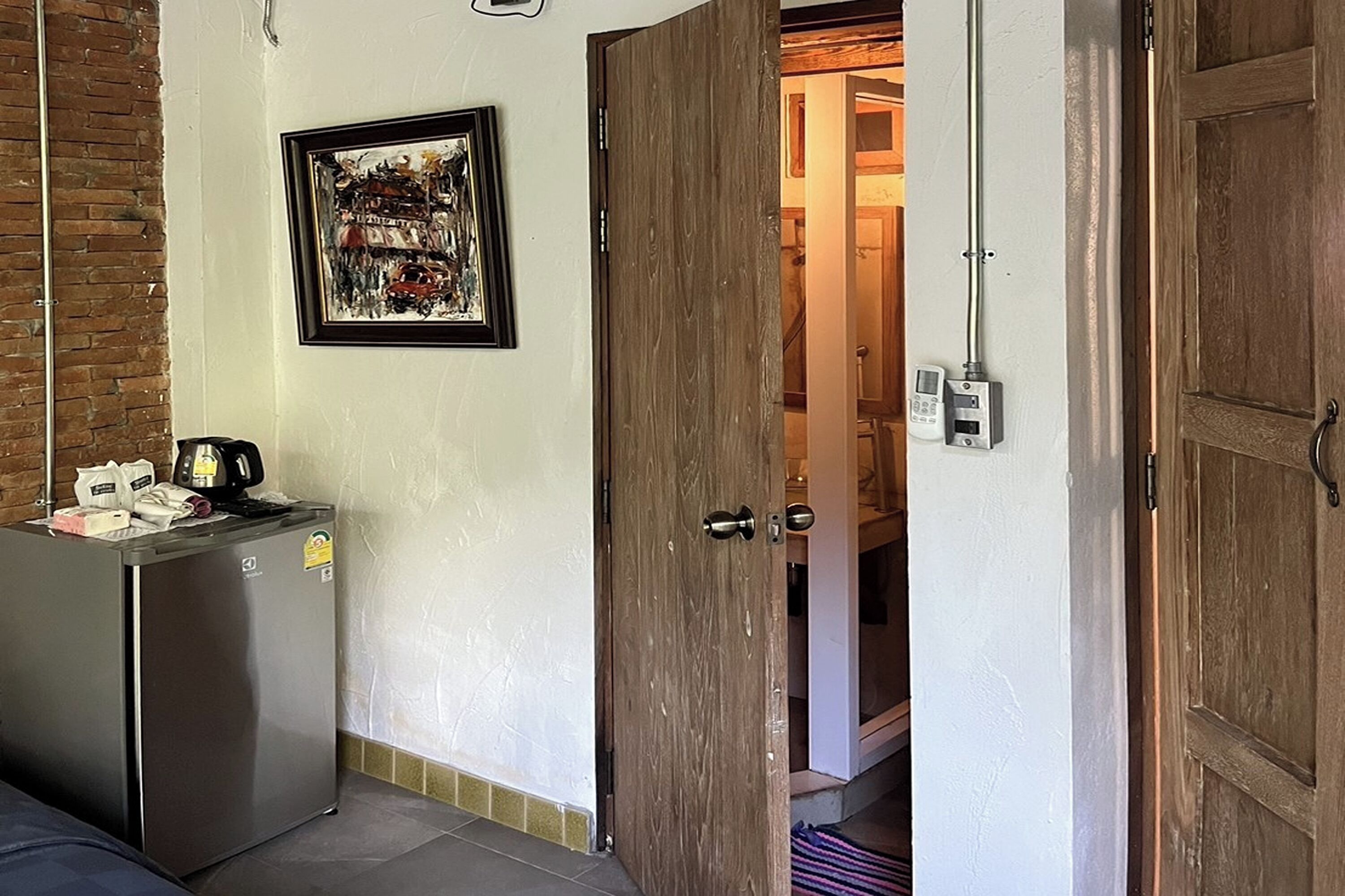 A room with a refrigerator, a wooden door, and a framed picture on the wall.