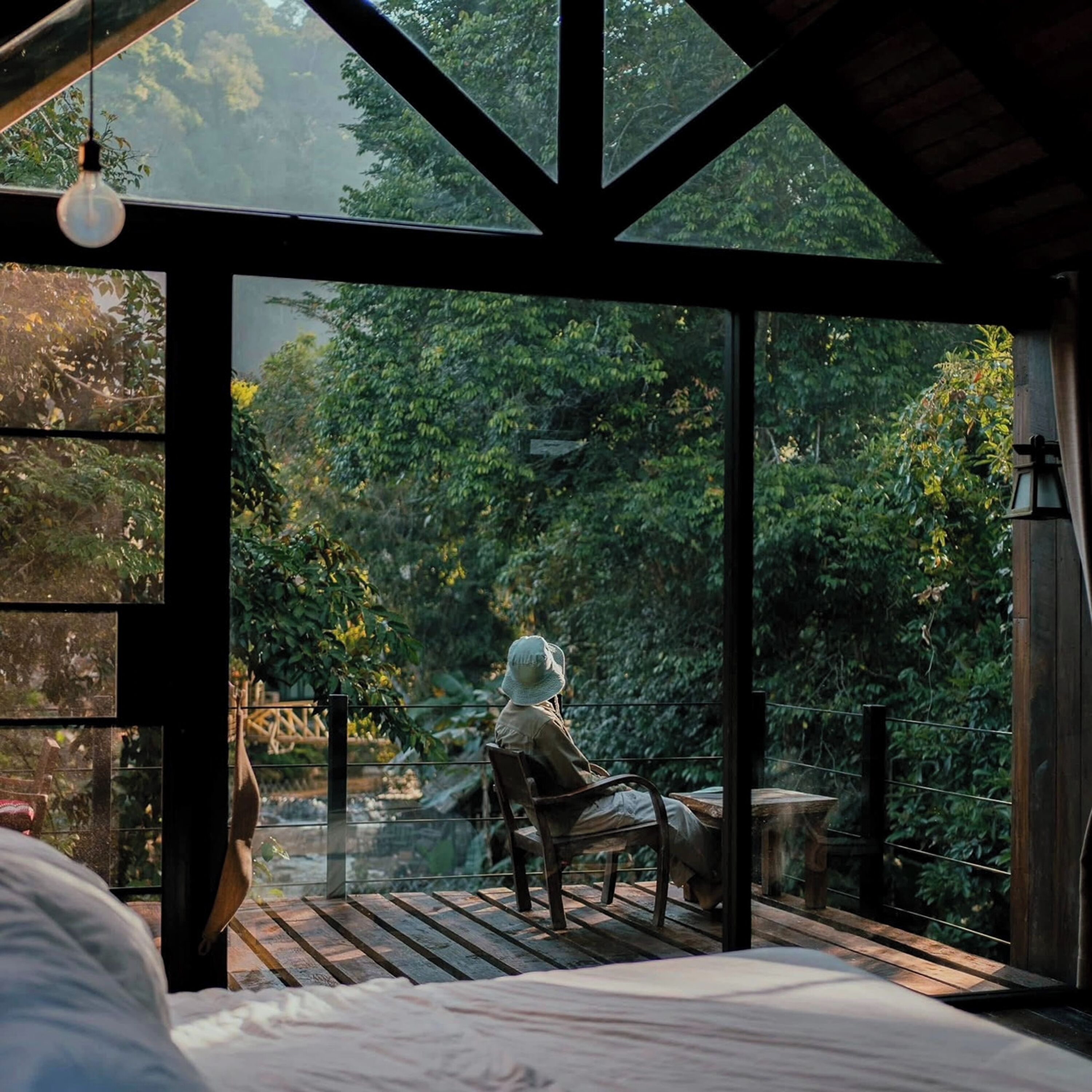 Ein Zimmer mit großem Fenster mit Blick auf einen Garten, eine Holzterrasse und eine Sitzecke mit Stuhl und Tisch.