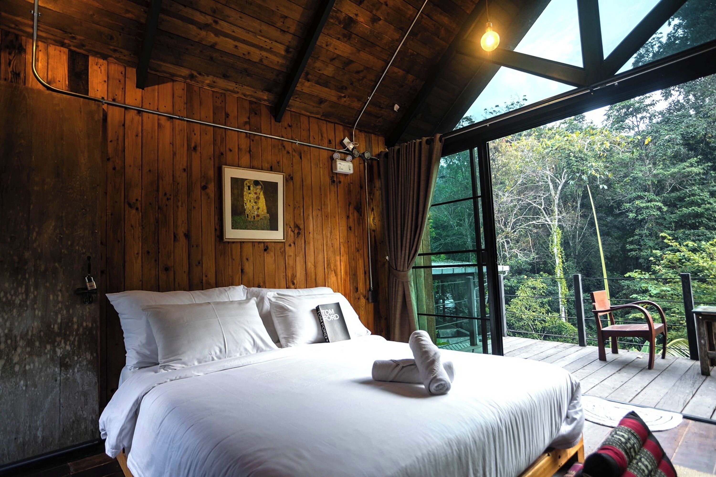Une chambre dans une cabane en bois, avec un grand lit, un tableau encadré au mur et une vue sur la forêt par la fenêtre.