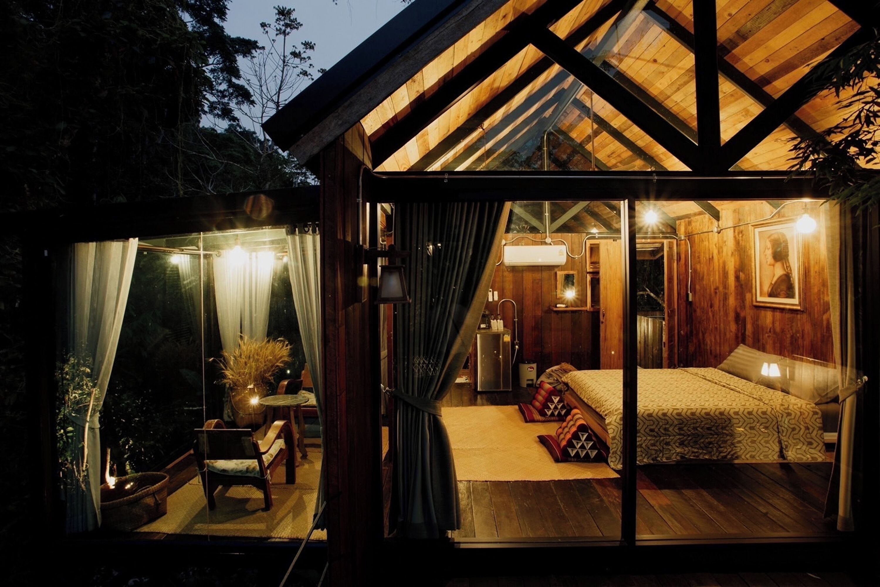 A cozy wooden cabin with a glass door leading to a bedroom with a bed, bedside table, and lamp.