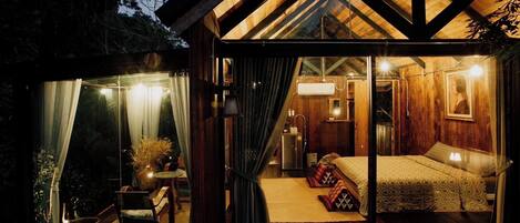 A cozy wooden cabin with a glass door leading to a bedroom with a bed, bedside table, and lamp.