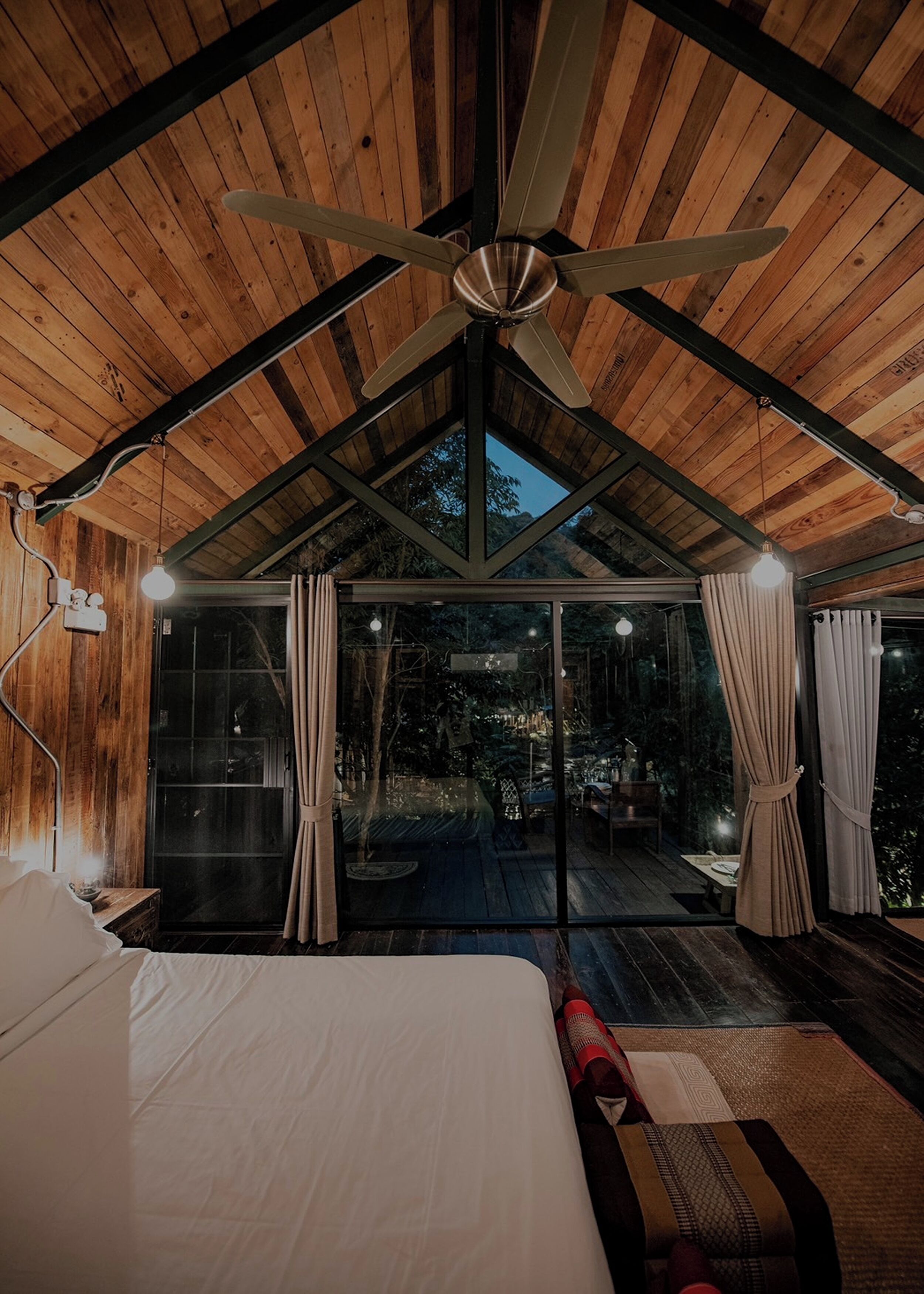 A bedroom with a large bed, a ceiling fan, and a glass door leading to an outdoor area.