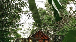 A multi-level wooden house surrounded by dense greenery and a stream. - Voraman Hut (Doi Saket)