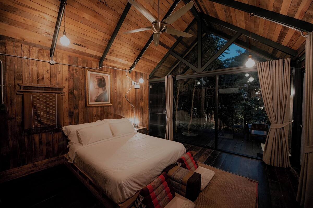 A wooden cabin bedroom with a bed, a ceiling fan, and a large window overlooking a deck.