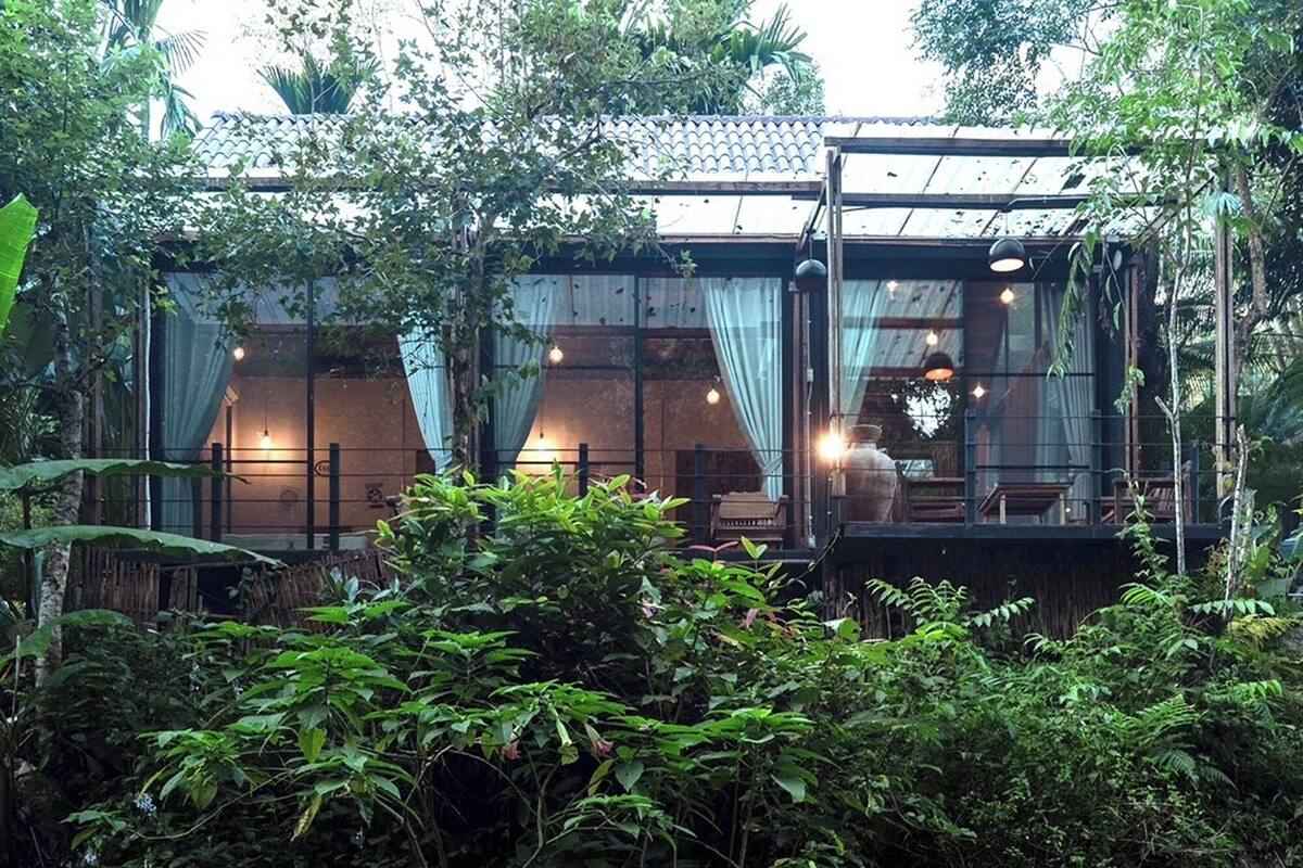 A riverside building with a glass facade, surrounded by dense greenery and a flowing river.