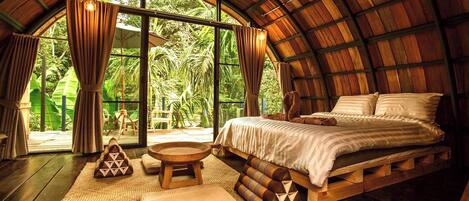 A bedroom with a wooden ceiling, a bed, a window, and a view of greenery outside.