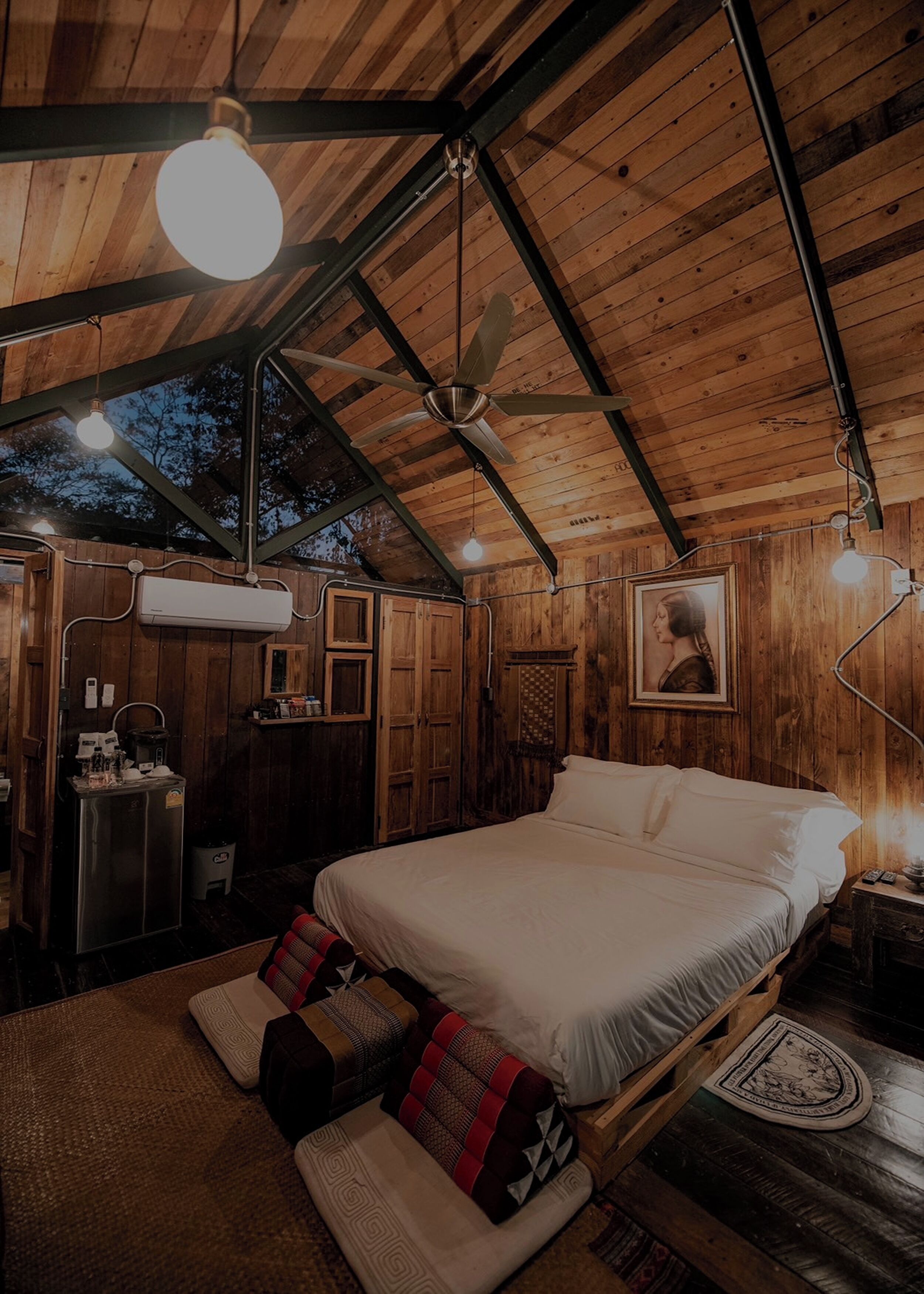 A cozy wooden cabin bedroom with a bed, pillows, a ceiling fan, and a nightstand.