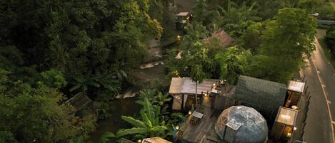 An aerial view of a resort with a river, dense greenery, and a large dome structure.