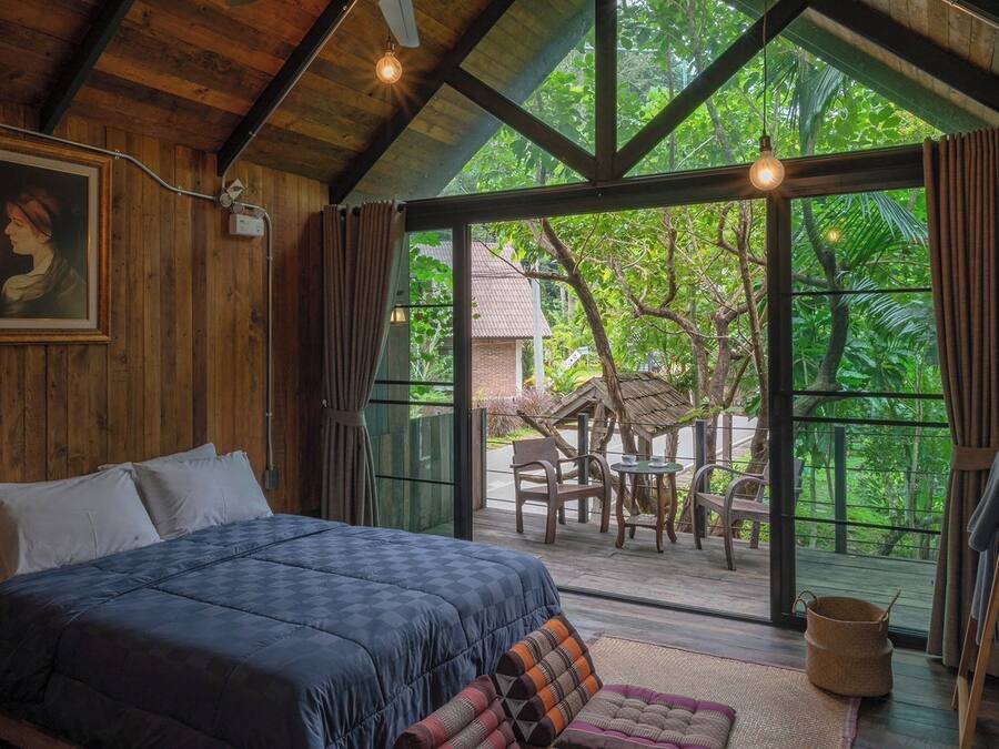 Un dormitorio con una cama grande, paredes de madera y vistas a un jardín tropical.