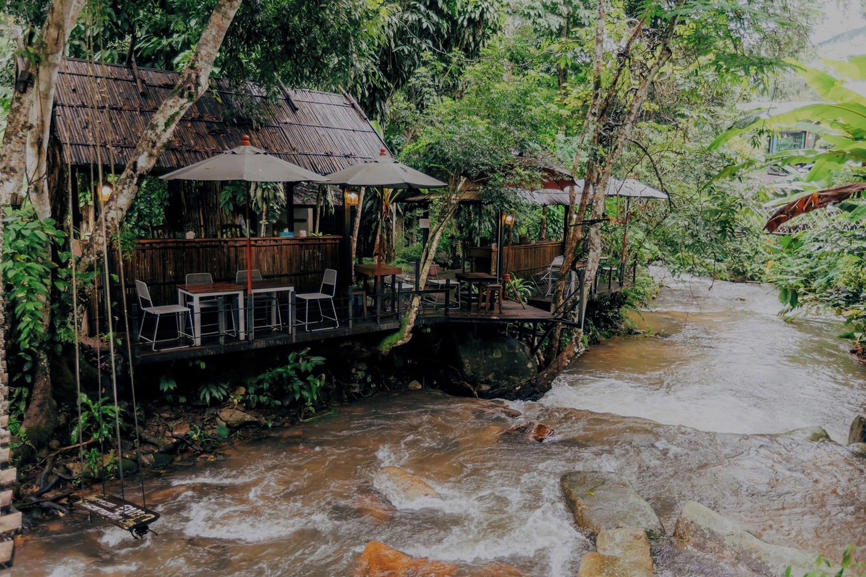 A riverside restaurant with outdoor seating, wooden tables, and umbrellas.