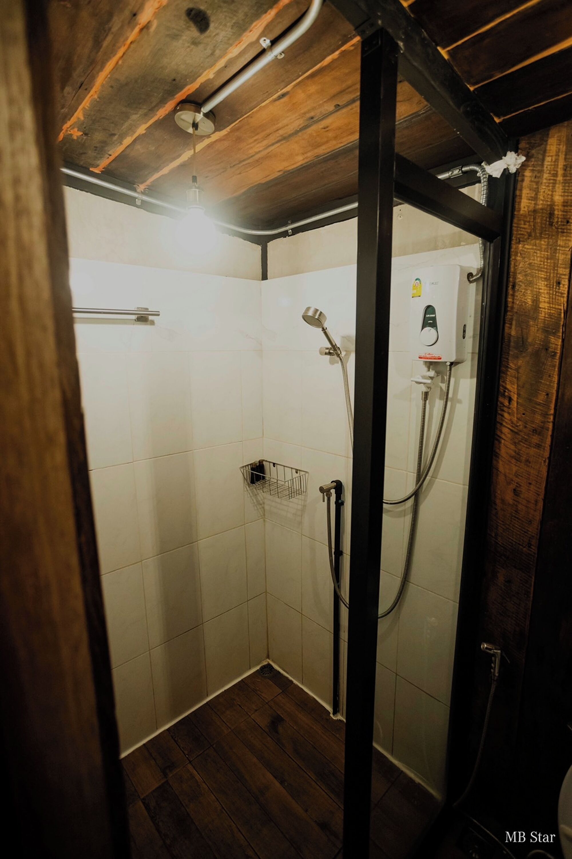 A small, enclosed shower area with white tiled walls and wooden flooring.