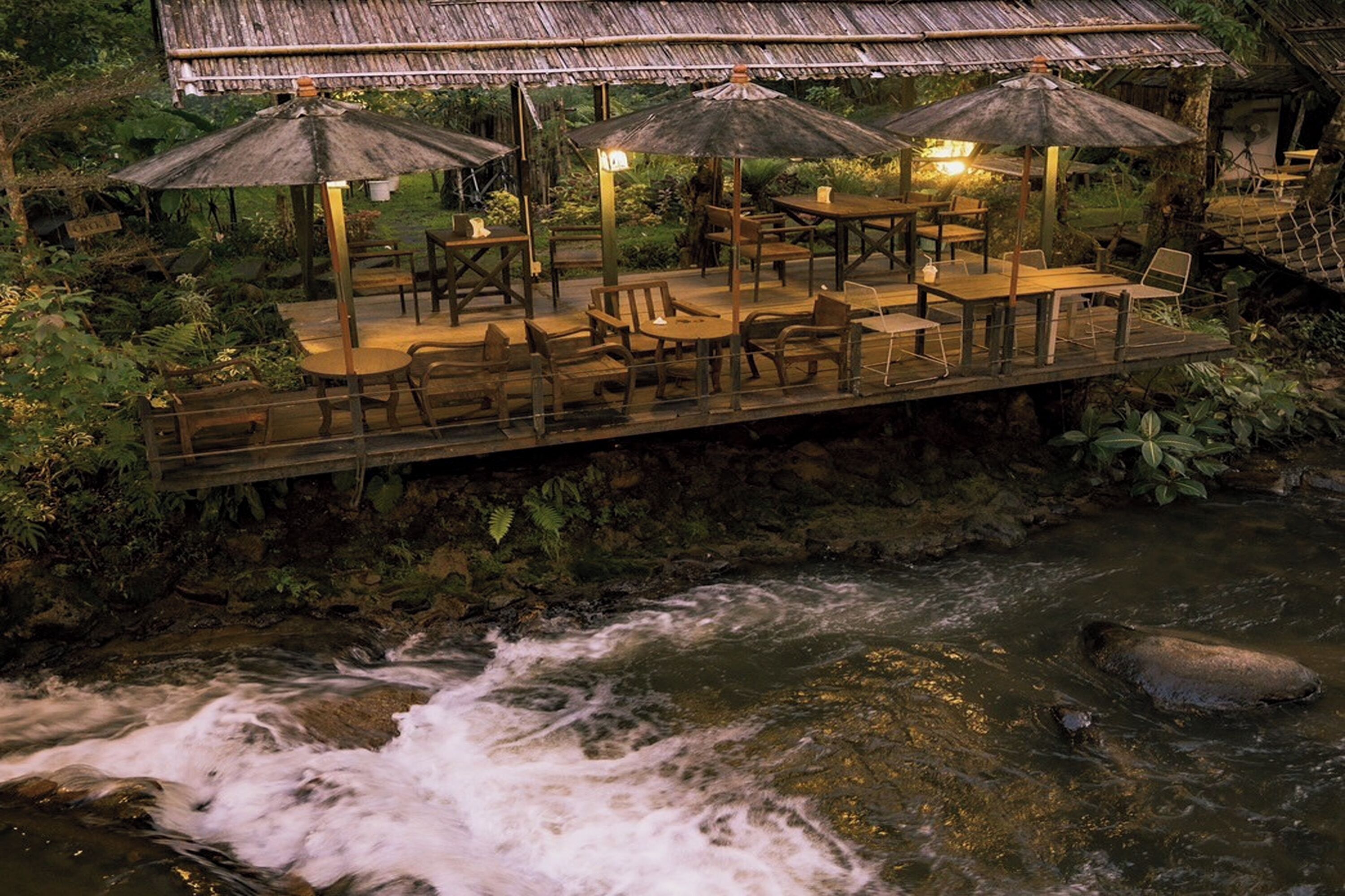 Una terraza de madera con mesas y sillas que da a un río caudaloso.