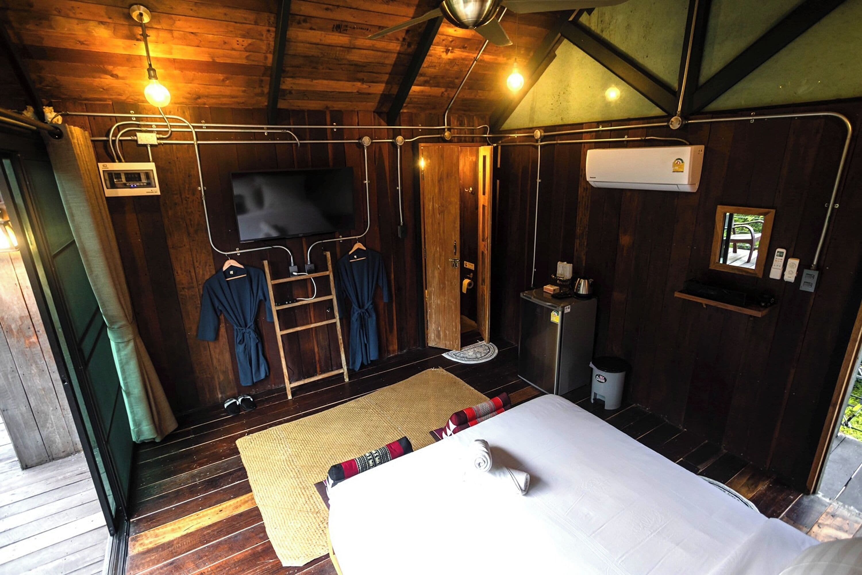 Ein Zimmer aus Holz mit einem Bett, einem Fernseher, einer kleinen Ablage und einem Fenster.