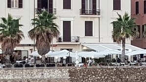 A building with multiple balconies and windows, palm trees in front, and outdoor seating with umbrellas. - Mowita seaside flat with stunning view on the sea (Civitavecchia)