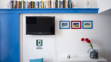 A room with a bookshelf, a flat-screen TV, framed pictures, a vase with flowers, and an emergency exit sign.