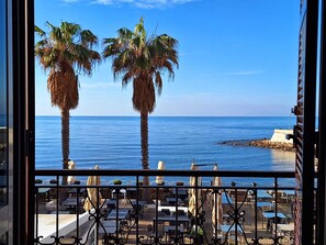 Un balcon avec vue sur la mer, des palmiers et des sièges d’extérieur.
