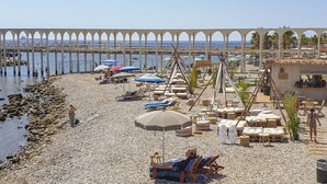 A beach with lounge chairs and umbrellas, a pier in the background, and a thatched-roof building. - Mowita seaside flat with stunning view on the sea (Civitavecchia)