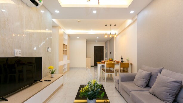A modern living room with a flat-screen TV, a coffee table with a plant, a sofa, and a dining area in the background. - Scenic Valley - Vina We Stay Apartment (Ho Chi Minh City)
