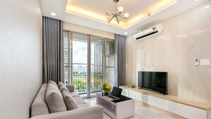 A modern living room with a sofa, a coffee table, a TV, and a balcony with curtains. - Scenic Valley - Vina We Stay Apartment (Ho Chi Minh City)