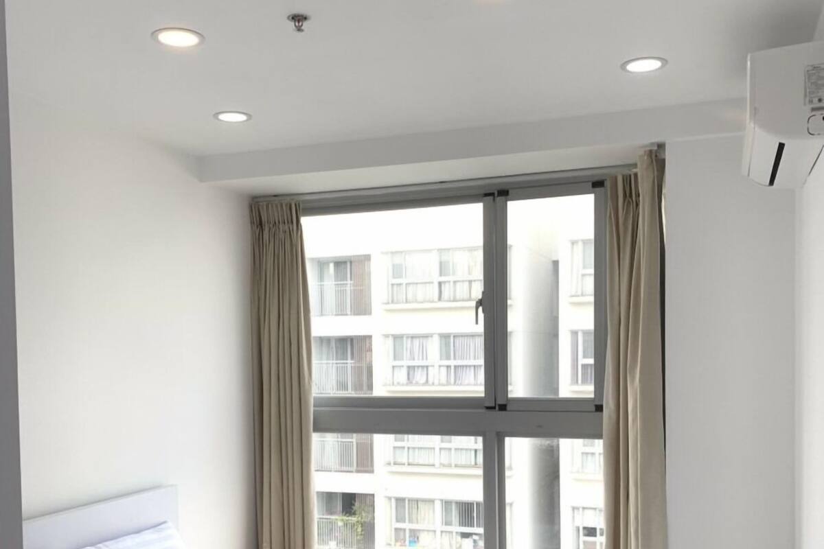A hotel room with a bed, a window with curtains, and a ceiling with recessed lighting.