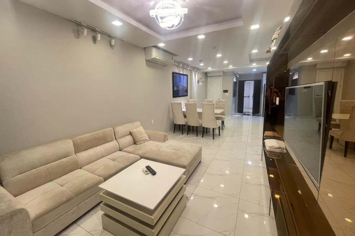 A modern living room with a sectional sofa, a coffee table, and a dining area with chairs and a TV.