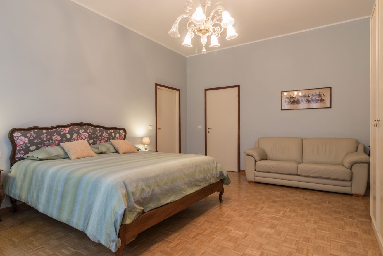 Quarto com cama, sofá, lustre e quadro na parede.