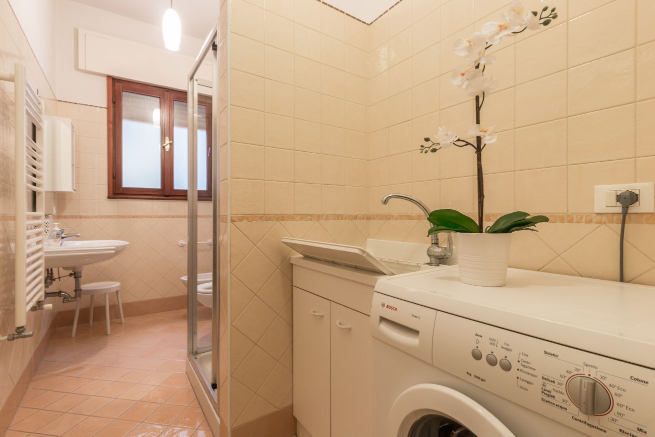 Un baño pequeño con lavadora, lavamanos y zona de ducha.