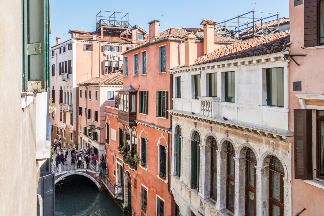 A narrow canal with buildings on either side, including a bridge with people walking.