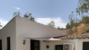 Un patio con piso de piedra, una mesa con sillas, una planta en maceta y un equipo de aire acondicionado.
