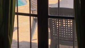 Una ventana con vista a un área exterior que incluye una piscina, sillas de descanso y vegetación.