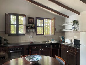 Une cuisine avec des meubles de rangement en bois, une cuisinière, un évier et une table à manger sur laquelle se trouve un saladier.