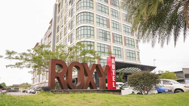 A hotel sign with the name "ROXY HOTEL" in front of a modern building with multiple floors and large windows.