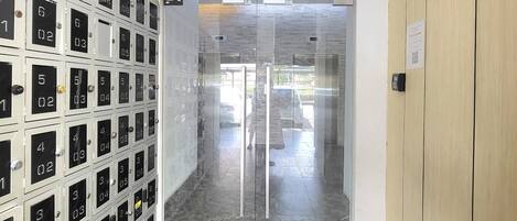 Entrada para o Roxy Apartment, com porta de vidro, uma fileira de caixas de correio numeradas e um armário de madeira à direita.