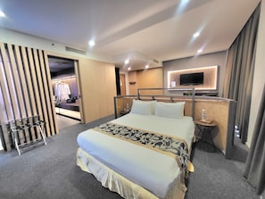 A modern hotel room with a large bed, a TV mounted on the wall, and a walk-in closet.