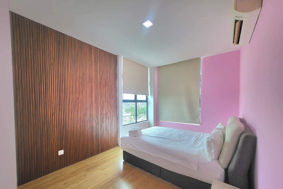 A bedroom with a wooden panel wall, a bed with pillows, a window with blinds, and a ceiling light.