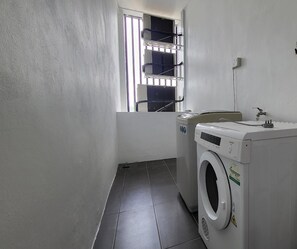 A laundry room with a washing machine, a dryer, and a window with bars. - Roxy Hotel 3rd Mile (Kuching)